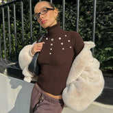 Person wearing a brown turtleneck sweater with silver buttons, holding a black handbag, and wearing a white fur coat.